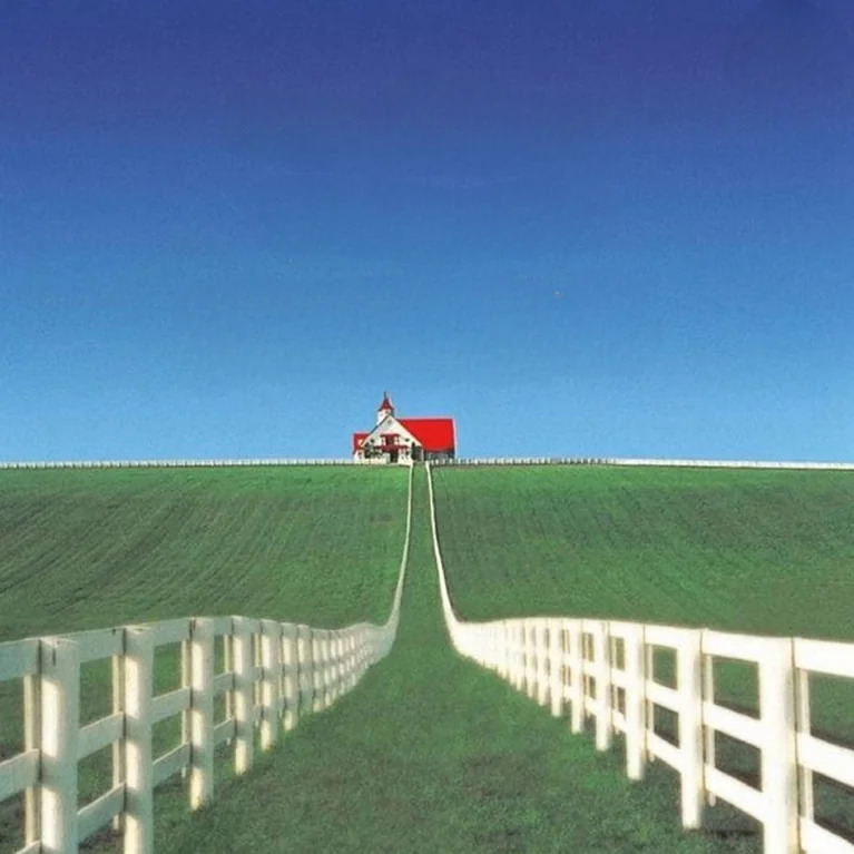 Some kind of building with a red roof and a long fence leading up to it